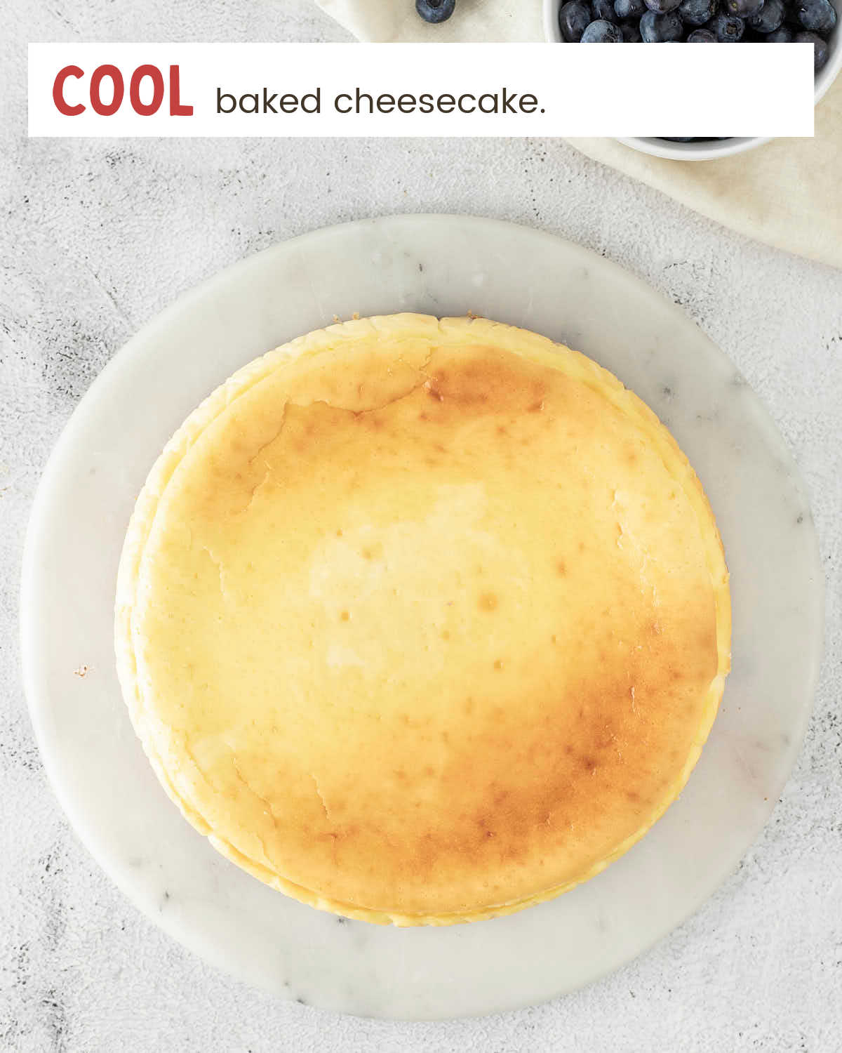 A plain baked cheesecake with a golden top on a marble board.