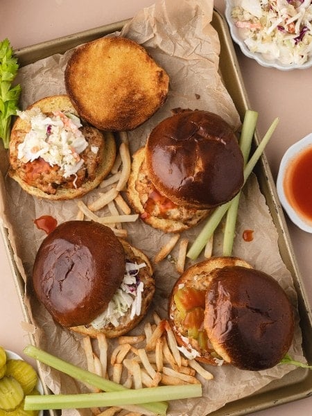 Overhead view of Buffalo Chicken Burgers on a sheet pan with fries and celery.