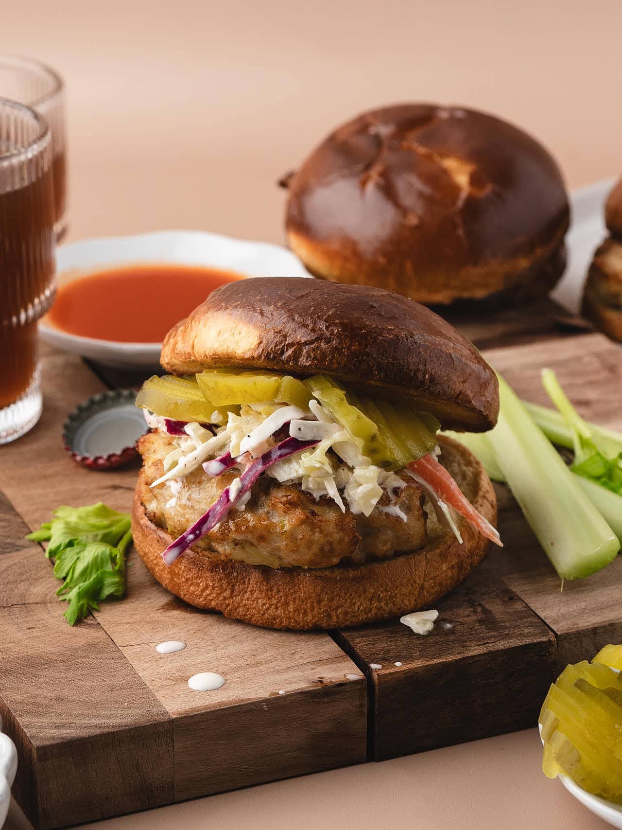 A Buffalo Chicken Burger topped with coleslaw and pickles on a wood board.