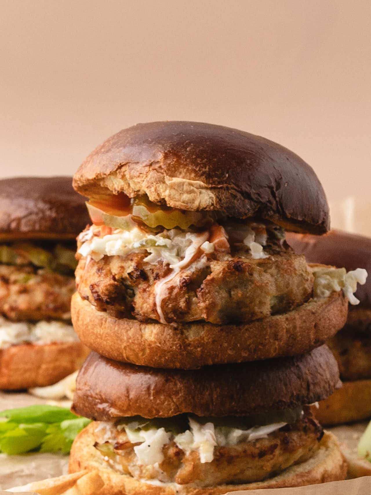 A close-up of stacked Buffalo Chicken Burgers with coleslaw and pickles.