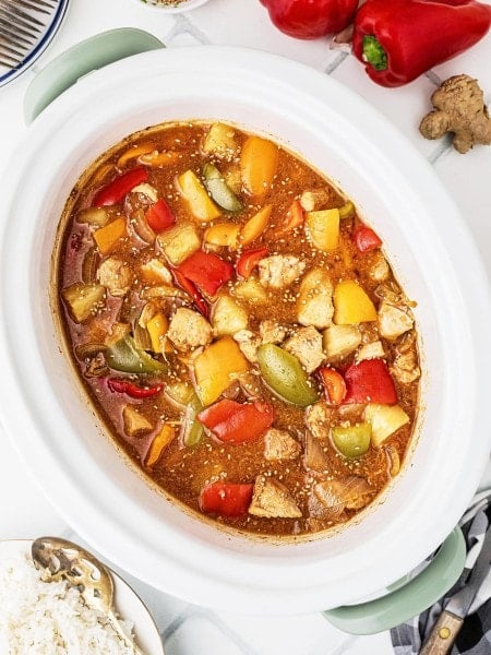 Crockpot Sweet and Sour Chicken with bell peppers and pineapple in a white slow cooker insert.