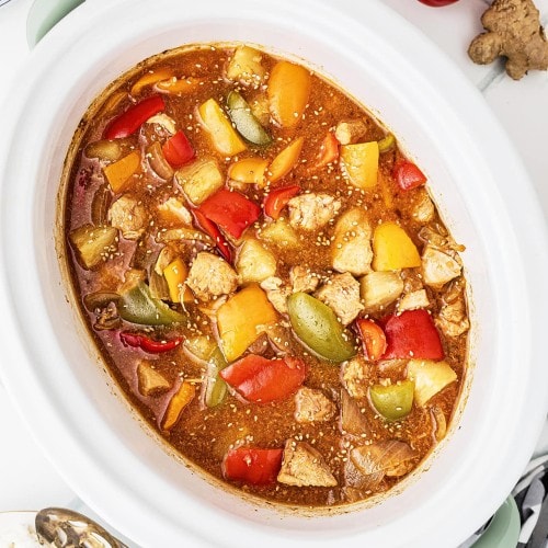 Crockpot Sweet and Sour Chicken with bell peppers and pineapple in a white slow cooker insert.