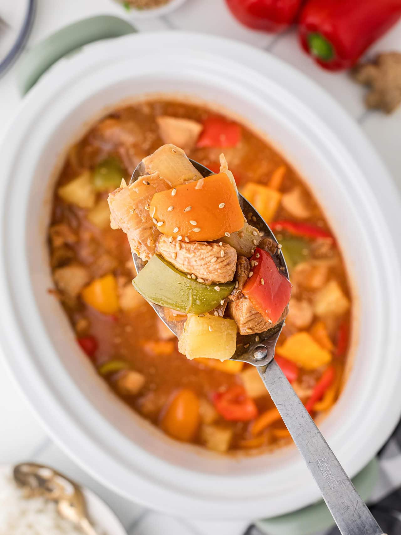 A serving spoon lifting Crockpot Sweet and Sour Chicken above the slow cooker.