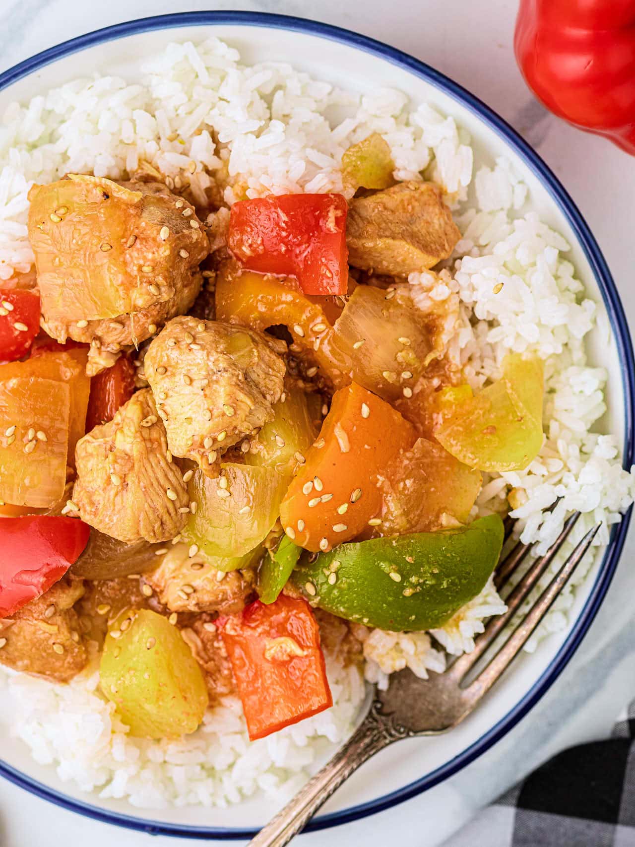 Overhead of a plated serving of Crockpot Sweet and Sour Chicken over white rice with a fork.