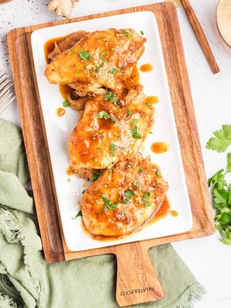 Honey Garlic Chicken Thighs on a white plate over rice with parsley.