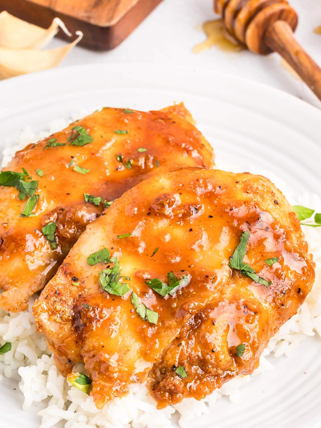 Honey Garlic Chicken Thighs over white rice with a honey dipper in the background.