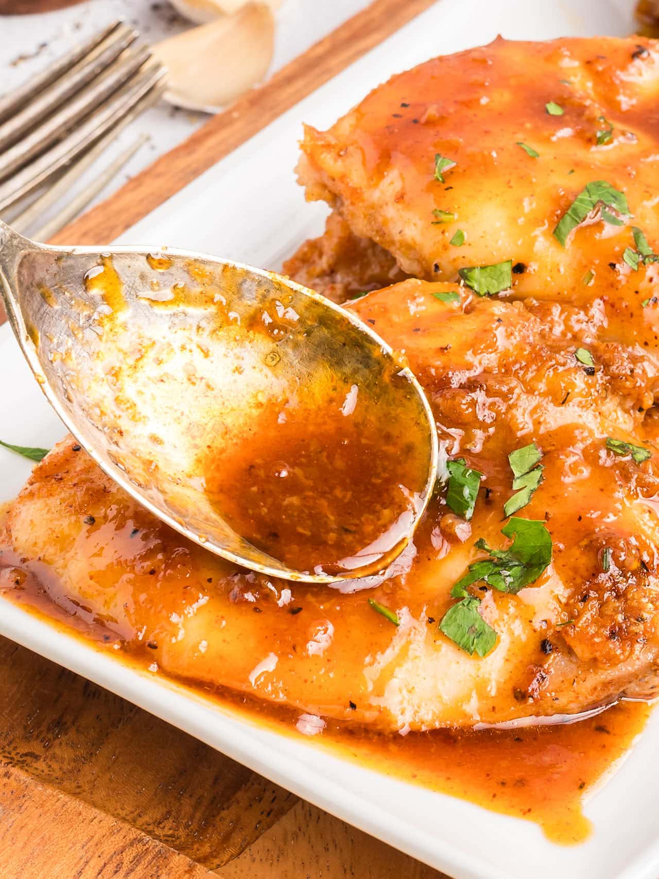 Honey Garlic Chicken Thighs on a platter with sauce being spooned over the top.