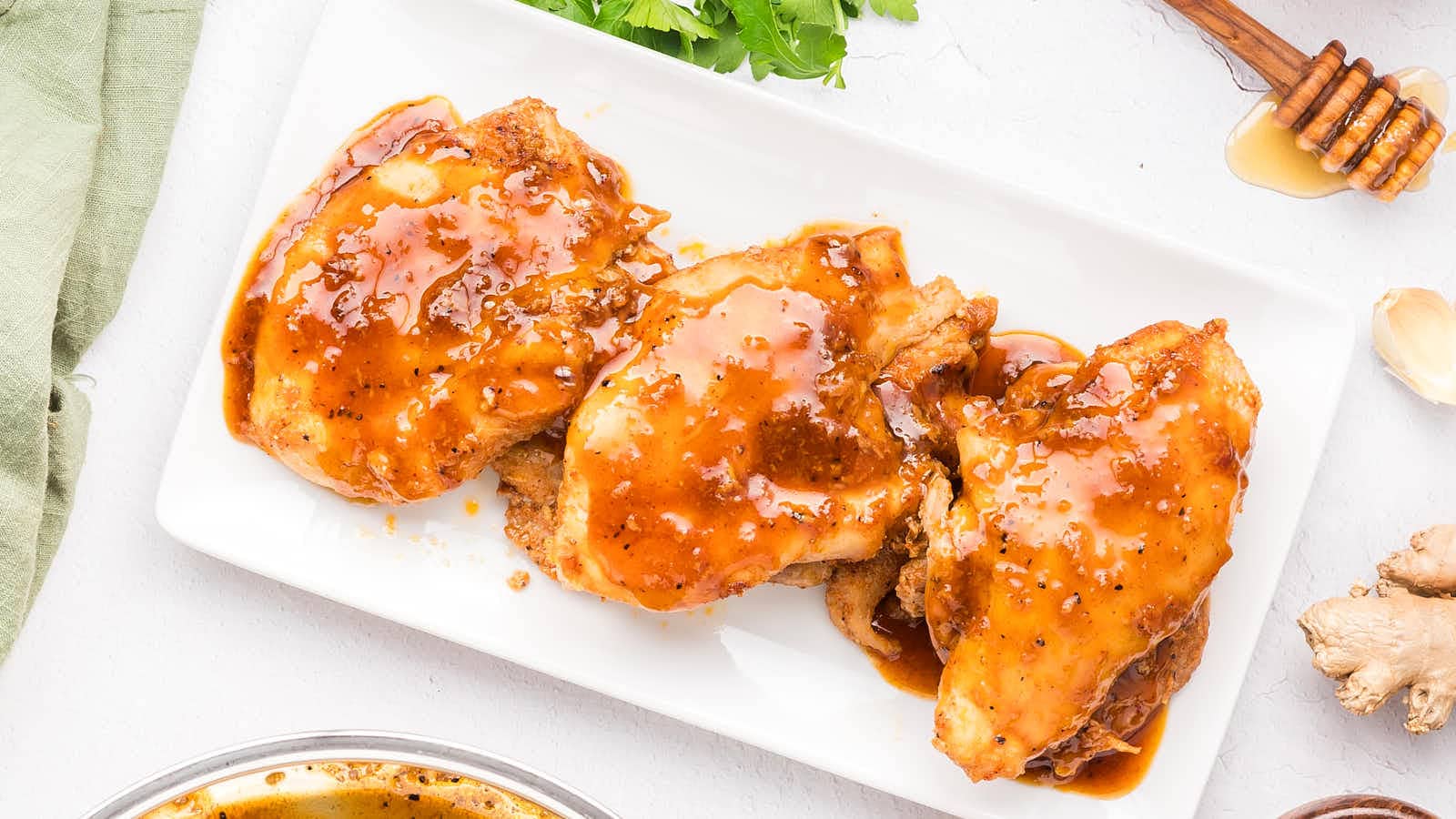 Honey Garlic Chicken Thighs coated in glossy sauce on a white platter, seen from above.