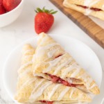 Two glazed Strawberry Turnovers on a white plate with fresh strawberries.