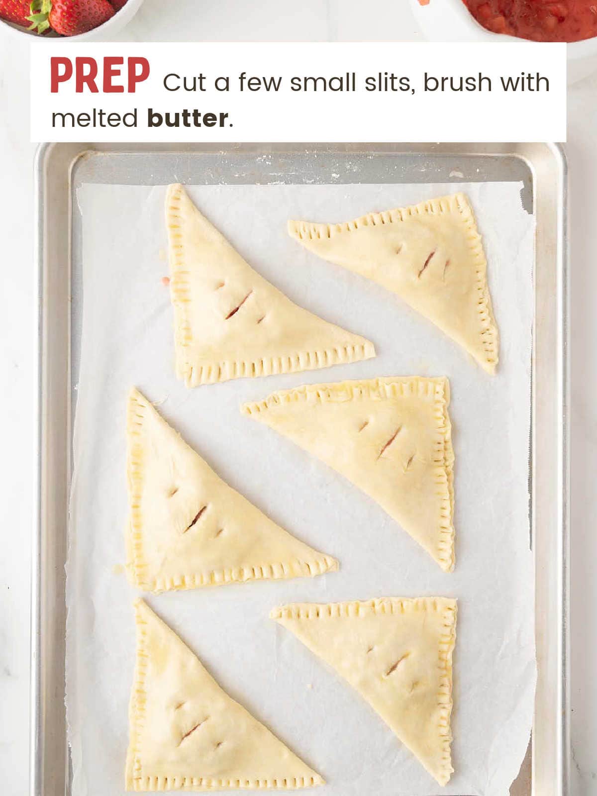 Folded and sealed Strawberry Turnovers with vented tops on a parchment-lined baking sheet.