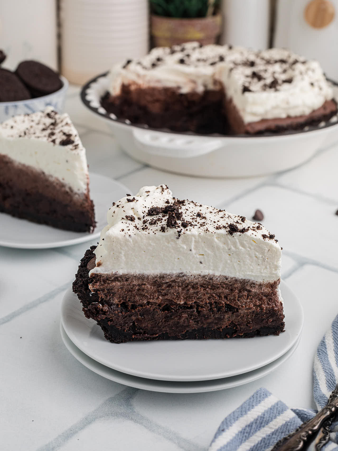 A tall slice of Mississippi Mud Pie on a white plate with the whole pie in the background.
