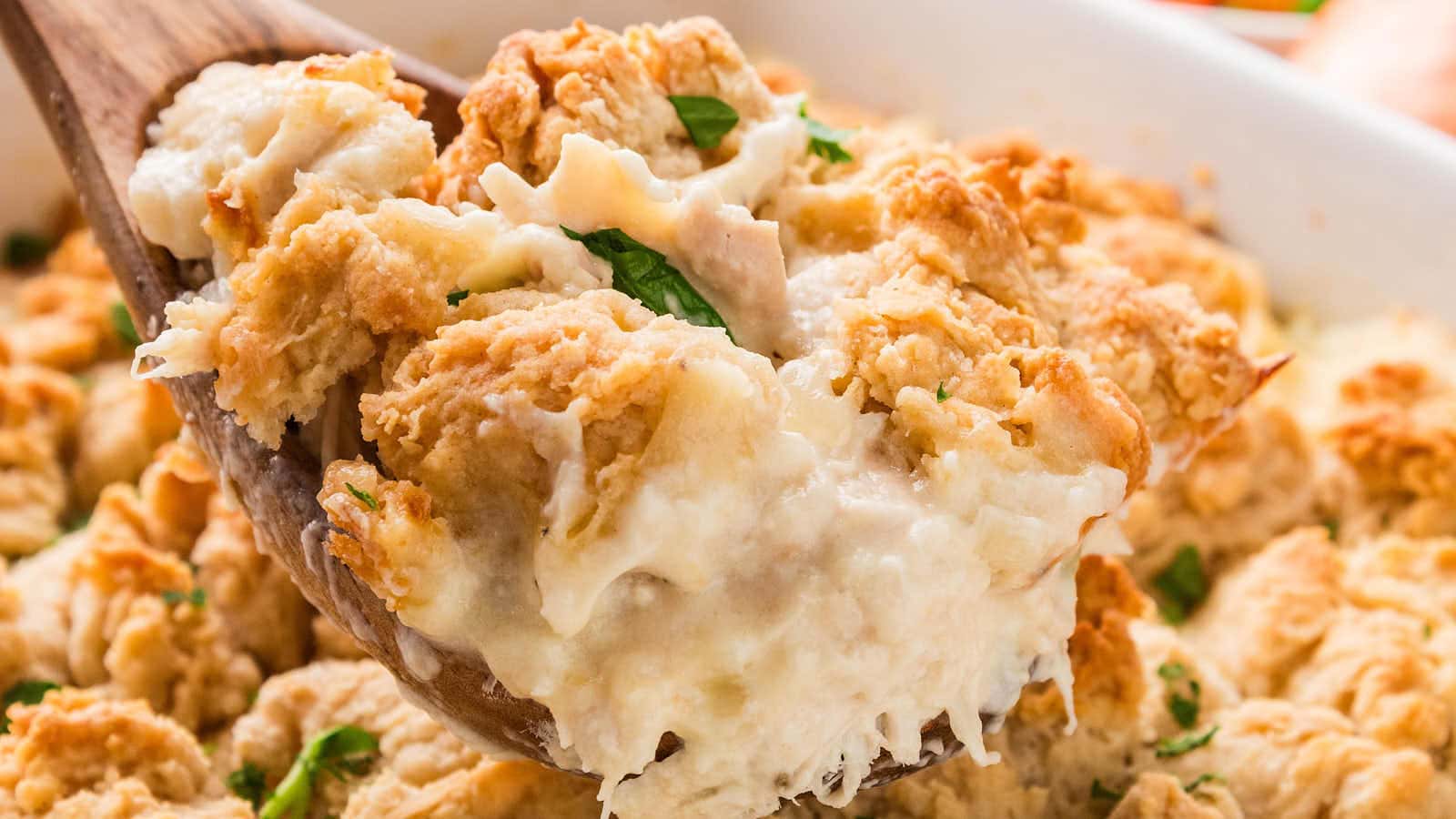 A wooden spoon scooping creamy Chicken Cobbler with a golden biscuit.