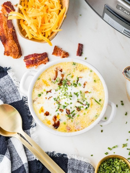 Crockpot Loaded Baked Potato Soup in a white bowl topped with bacon, cheddar, and chives.