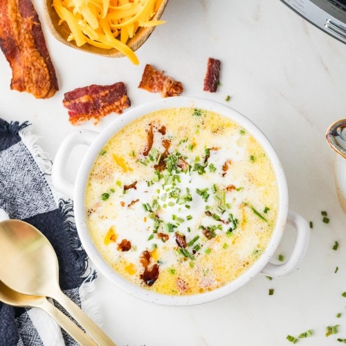 Crockpot Loaded Baked Potato Soup in a white bowl topped with bacon, cheddar, and chives.
