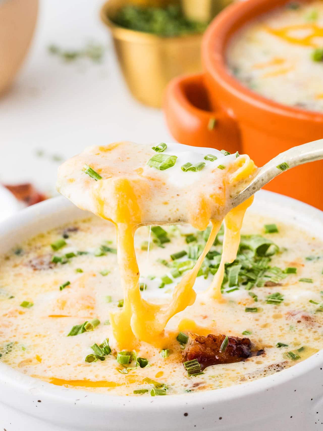 Spoonful of Crockpot Loaded Potato Soup with melted cheddar pulling from the bowl.
