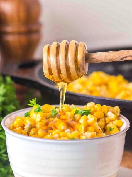 A honey dipper drizzling over a full bowl of Honey Butter Skillet Corn.