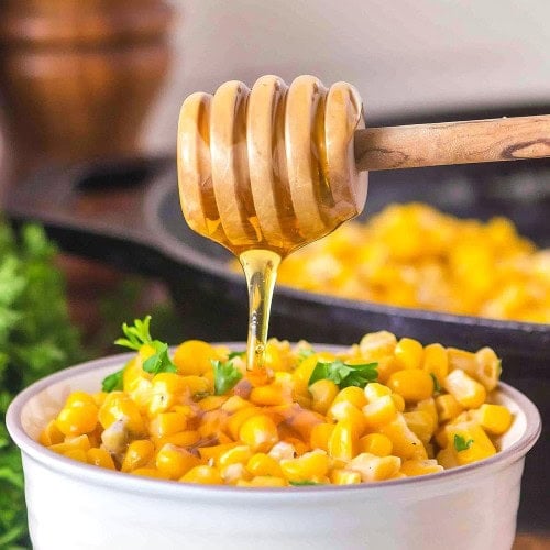A honey dipper drizzling over a full bowl of Honey Butter Skillet Corn.