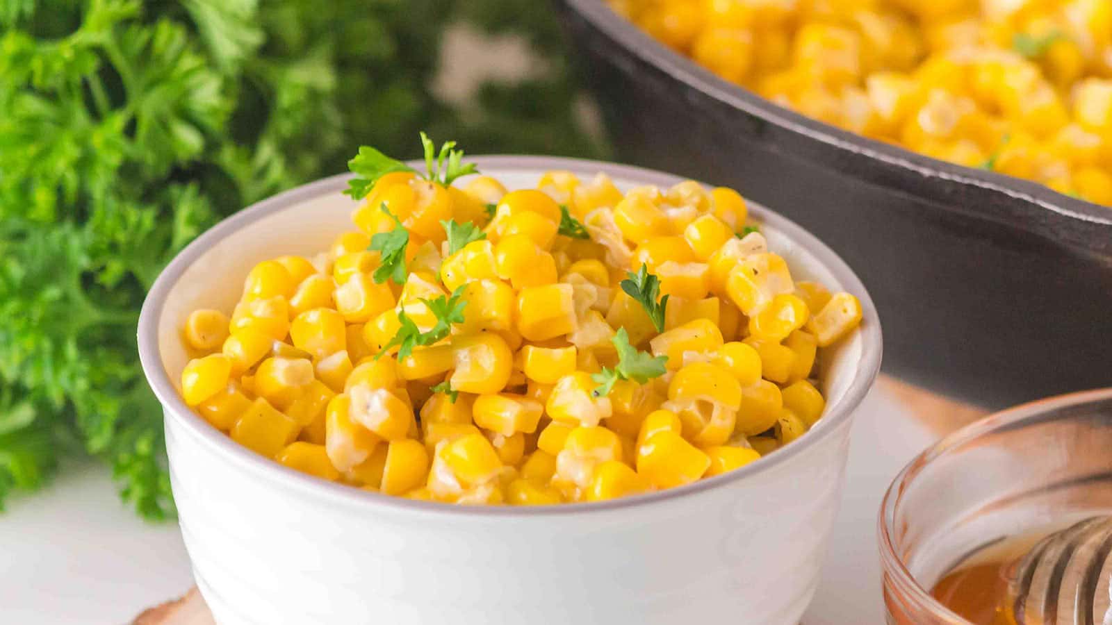 A bowl of Honey Butter Skillet Corn with a cast iron skillet behind it.