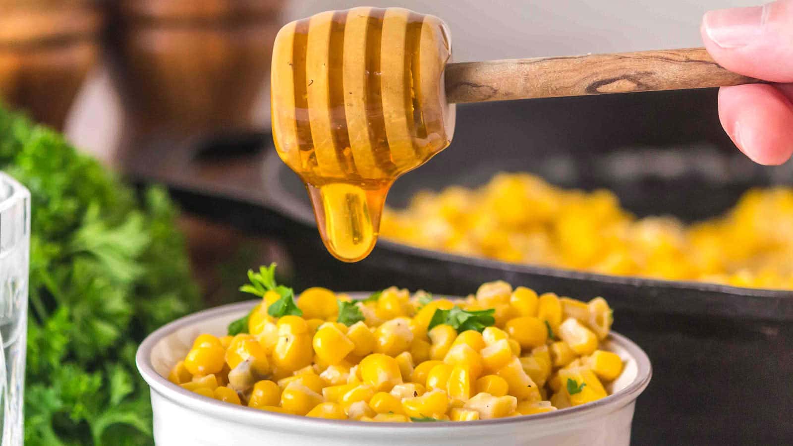 Honey dripping from a dipper over a bowl of Honey Butter Skillet Corn.