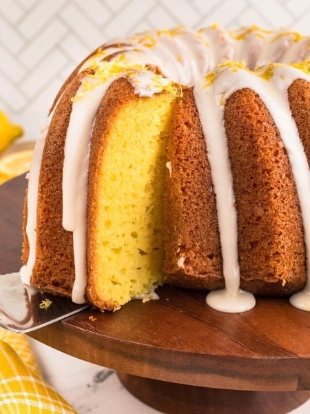 Cake server lifting the first slice from a glazed Lemon Bundt Cake.