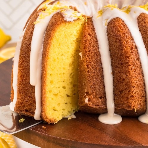 Cake server lifting the first slice from a glazed Lemon Bundt Cake.