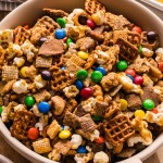 Sweet and Salty Chex Mix in a bowl with pretzels, popcorn, cashews, and colorful M&Ms.