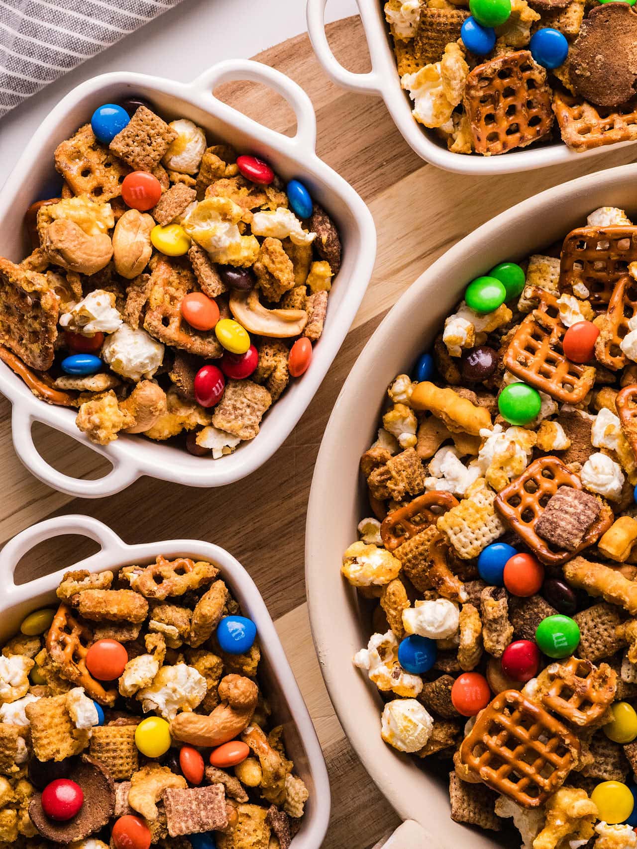 A wooden spoon resting in a dish of Sweet and Salty Chex Mix with colorful M&Ms.
