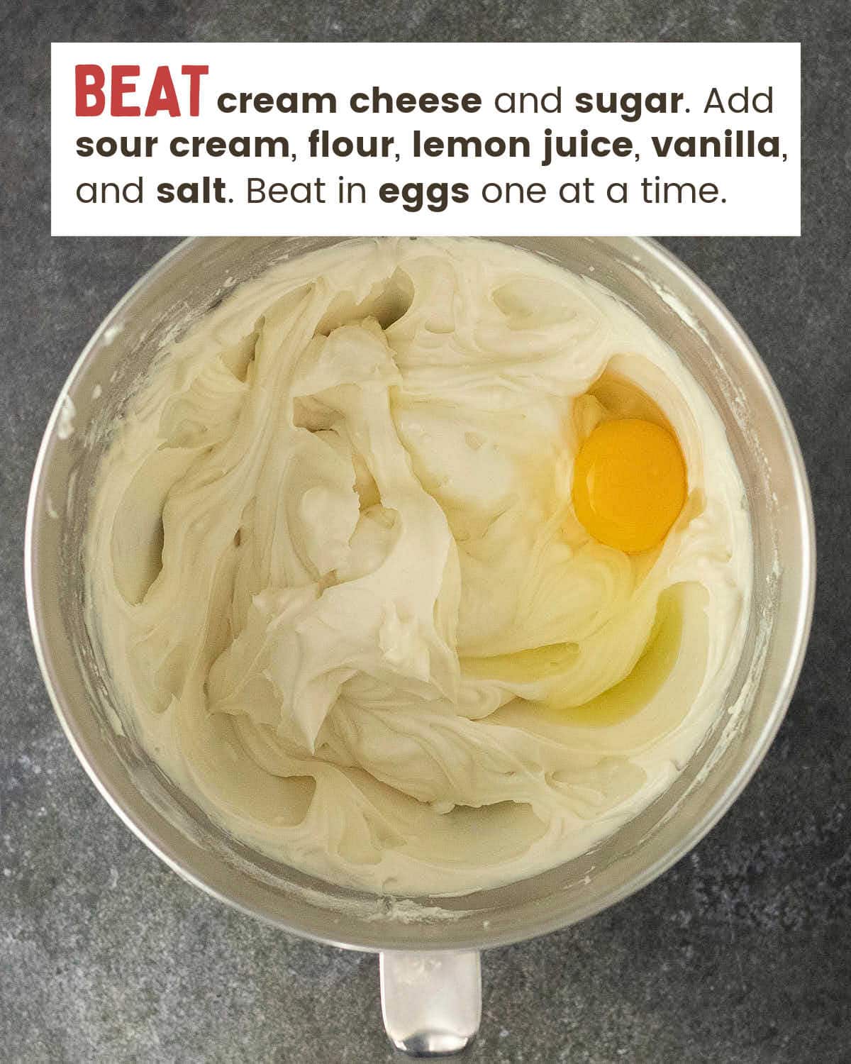 An egg added to the cheesecake filling in a stand mixer bowl.