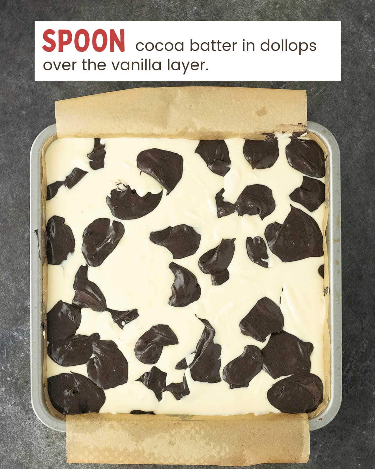 Spoonfuls of black cocoa batter dotted over the vanilla layer in the pan.