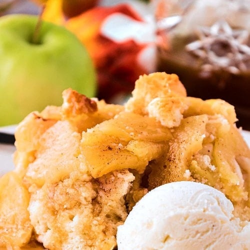 A serving of Apple Cobbler with vanilla ice cream, apples, and caramel sauce in the background.