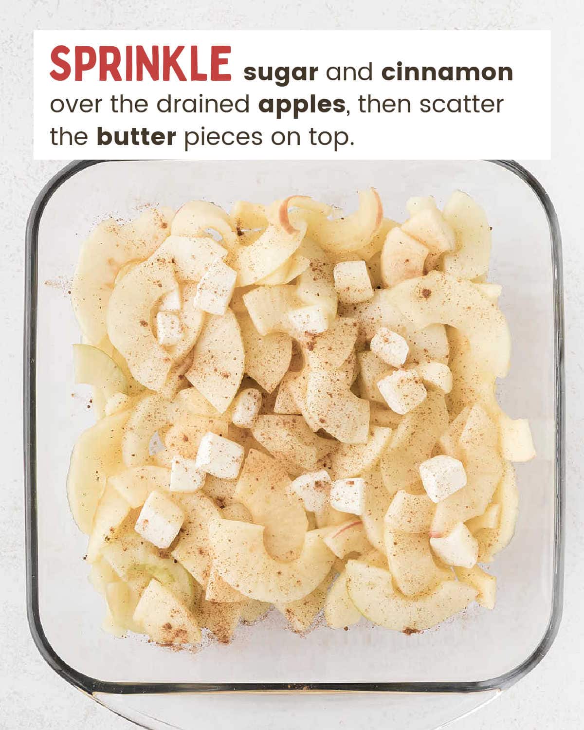 Apple slices in a baking dish sprinkled with sugar and cinnamon and topped with butter pieces.