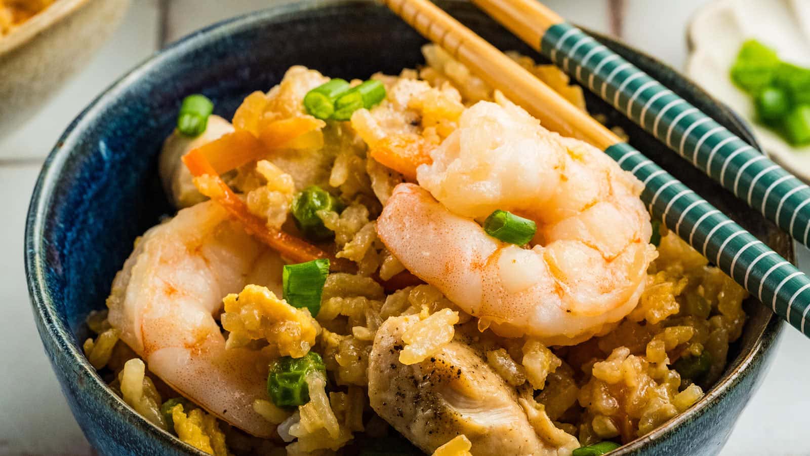 A blue bowl of Chicken and Shrimp Fried Rice with chopsticks resting on top.