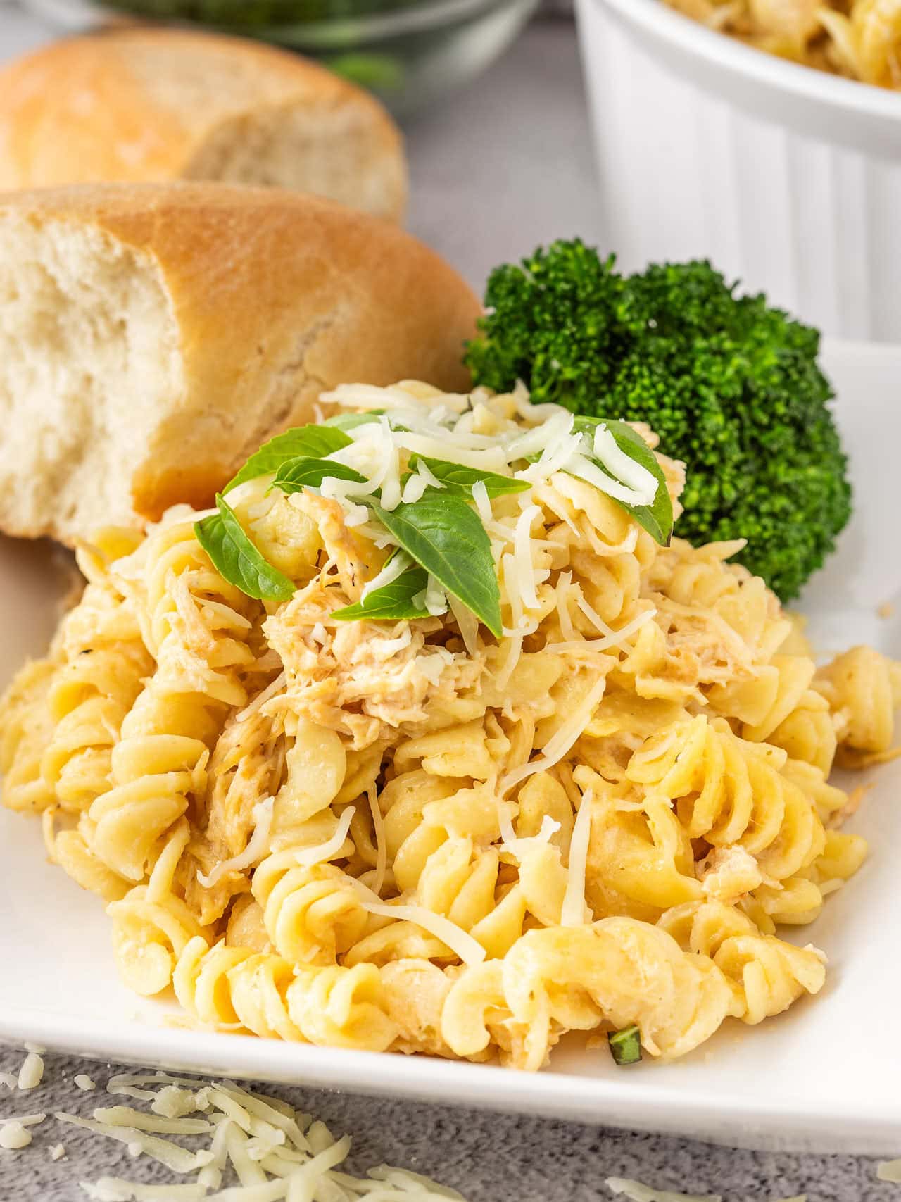 Olive Garden Chicken Pasta topped with fresh basil, served with a dinner roll and broccoli.