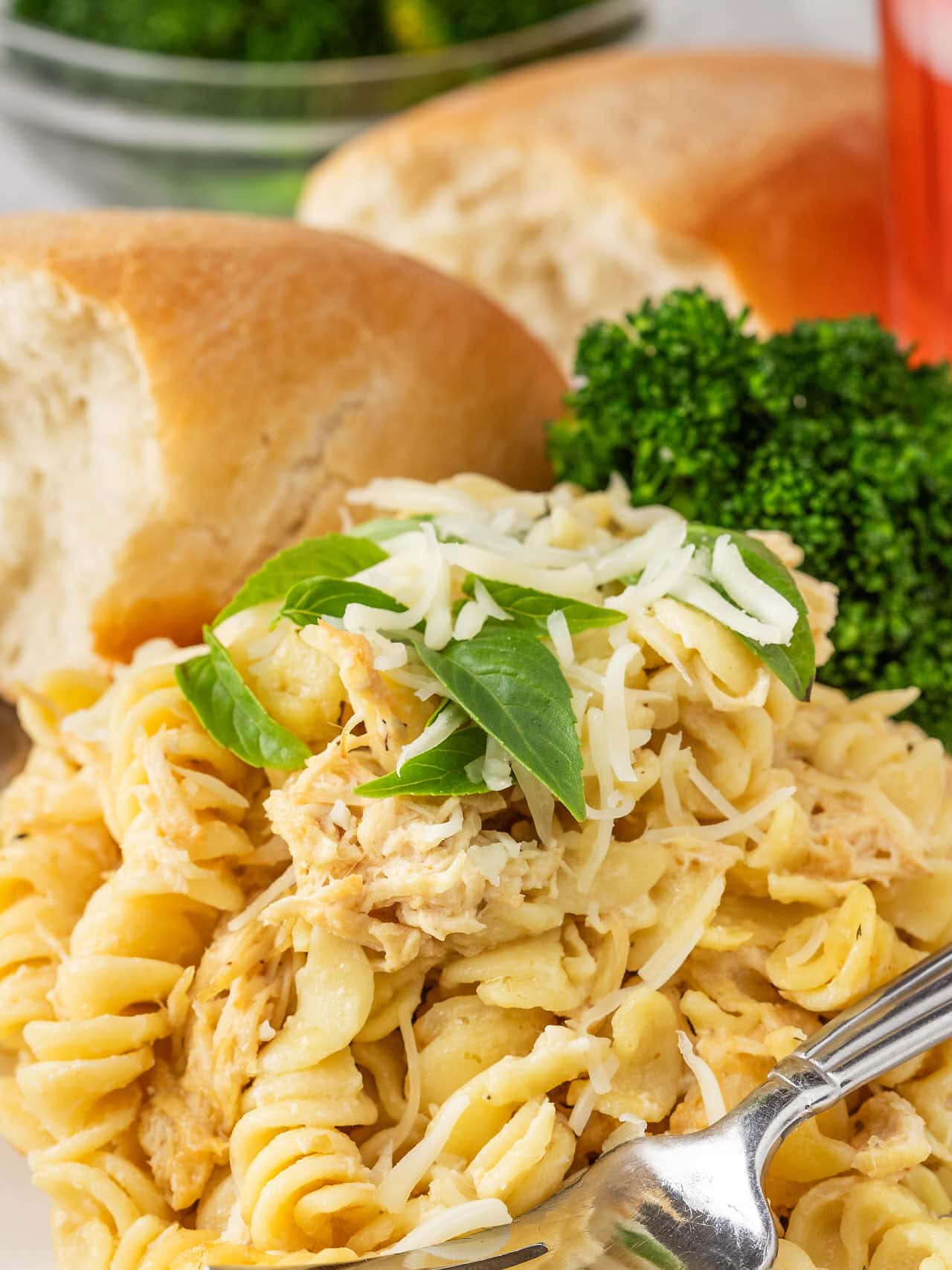 A dinner plate of Olive Garden Chicken Pasta with soft rolls and broccoli.