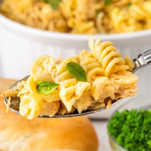 A heaping spoonful of Olive Garden Chicken Pasta held over the serving bowl.