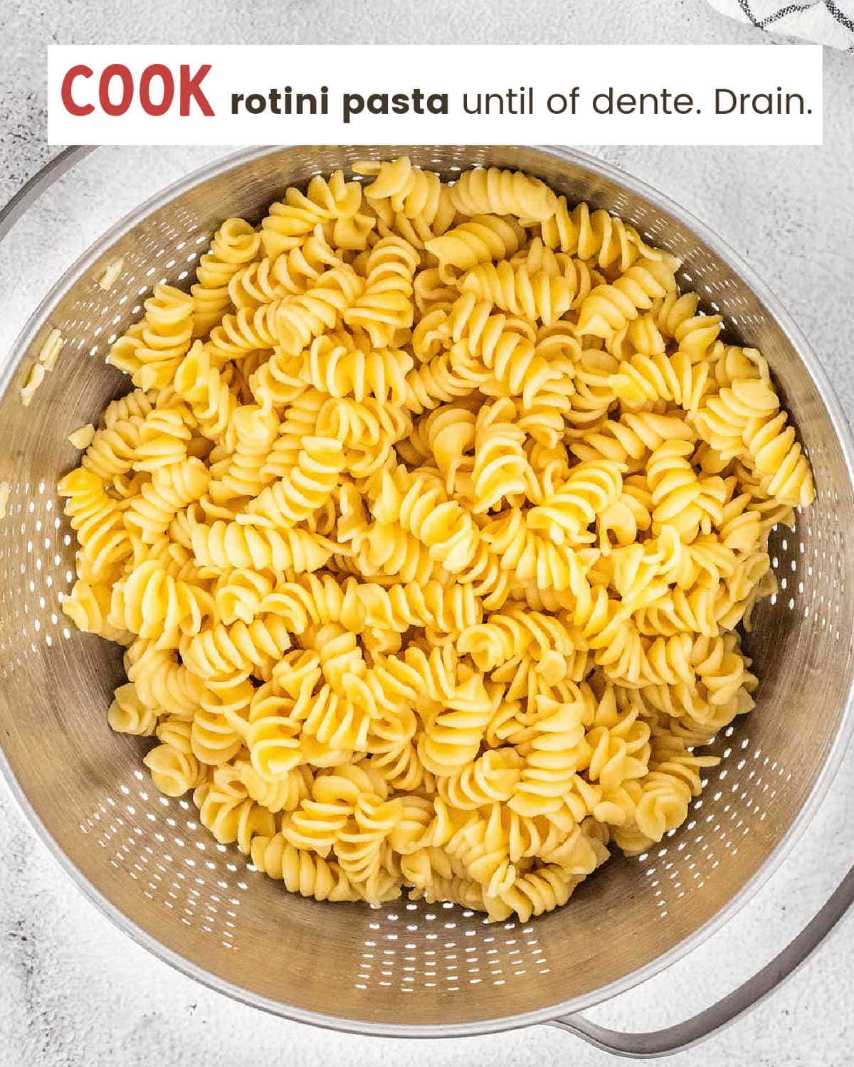 Cooked rotini pasta draining in a metal colander.