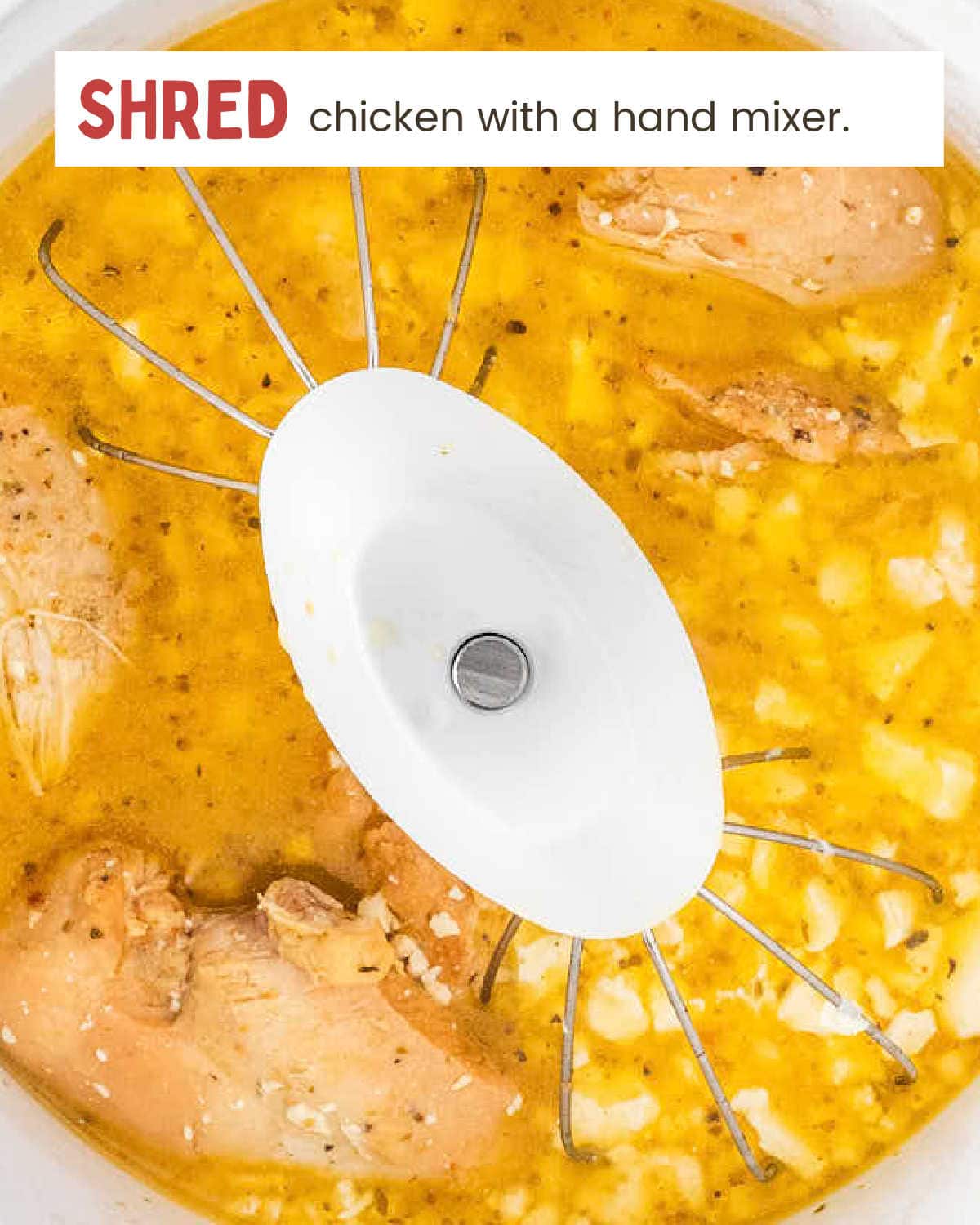 Shredding the cooked chicken in the pot with a hand mixer.