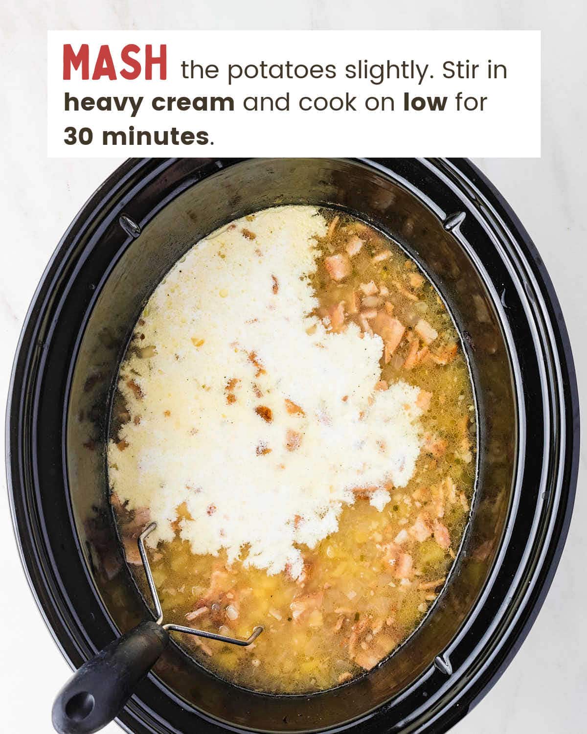 Heavy cream poured over mashed Crockpot Loaded Baked Potato Soup with a potato masher in the slow cooker.