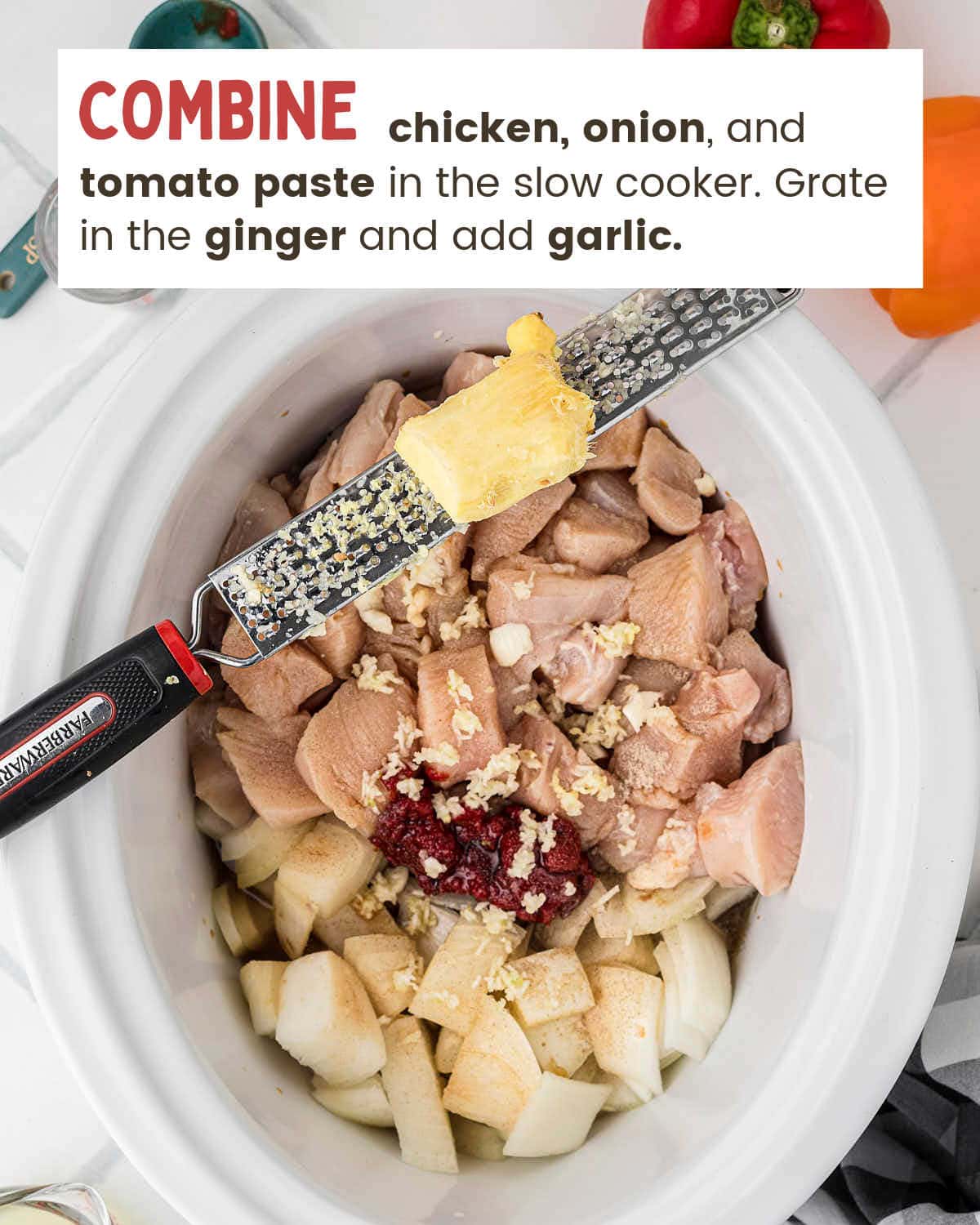 Grating fresh ginger over cubed chicken, onion, and tomato paste in the slow cooker.