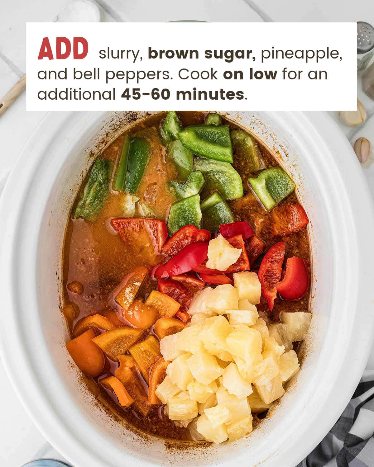 Pineapple chunks and bell peppers added to the cooked chicken in the slow cooker.