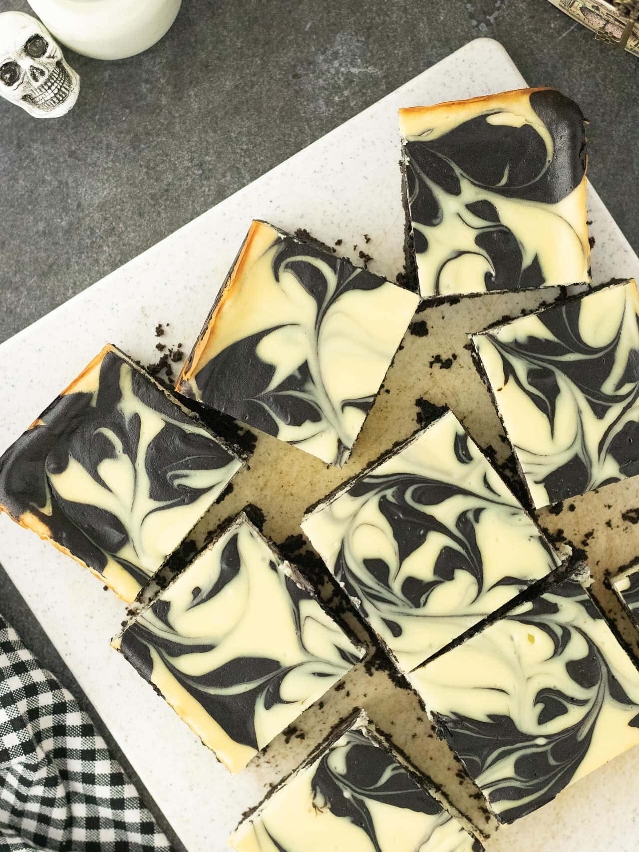 Sliced Halloween Cheesecake Bars arranged on a white platter with a skull decoration.