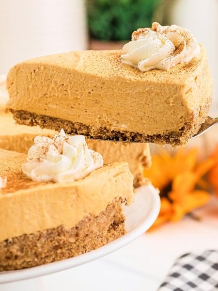 A slice of No Bake Pumpkin Cheesecake on a cake server with the whole dessert below.