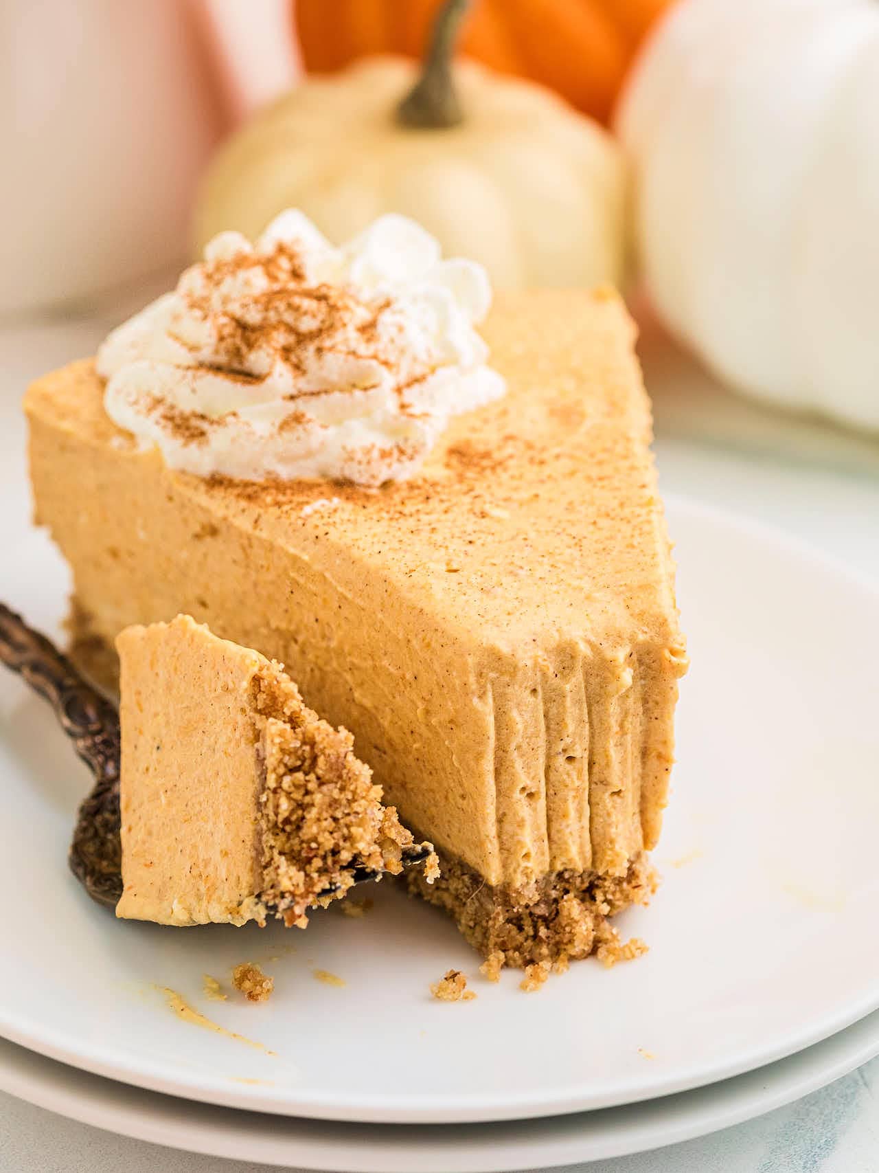 A forkful of No Bake Pumpkin Cheesecake resting against the slice on a white plate.