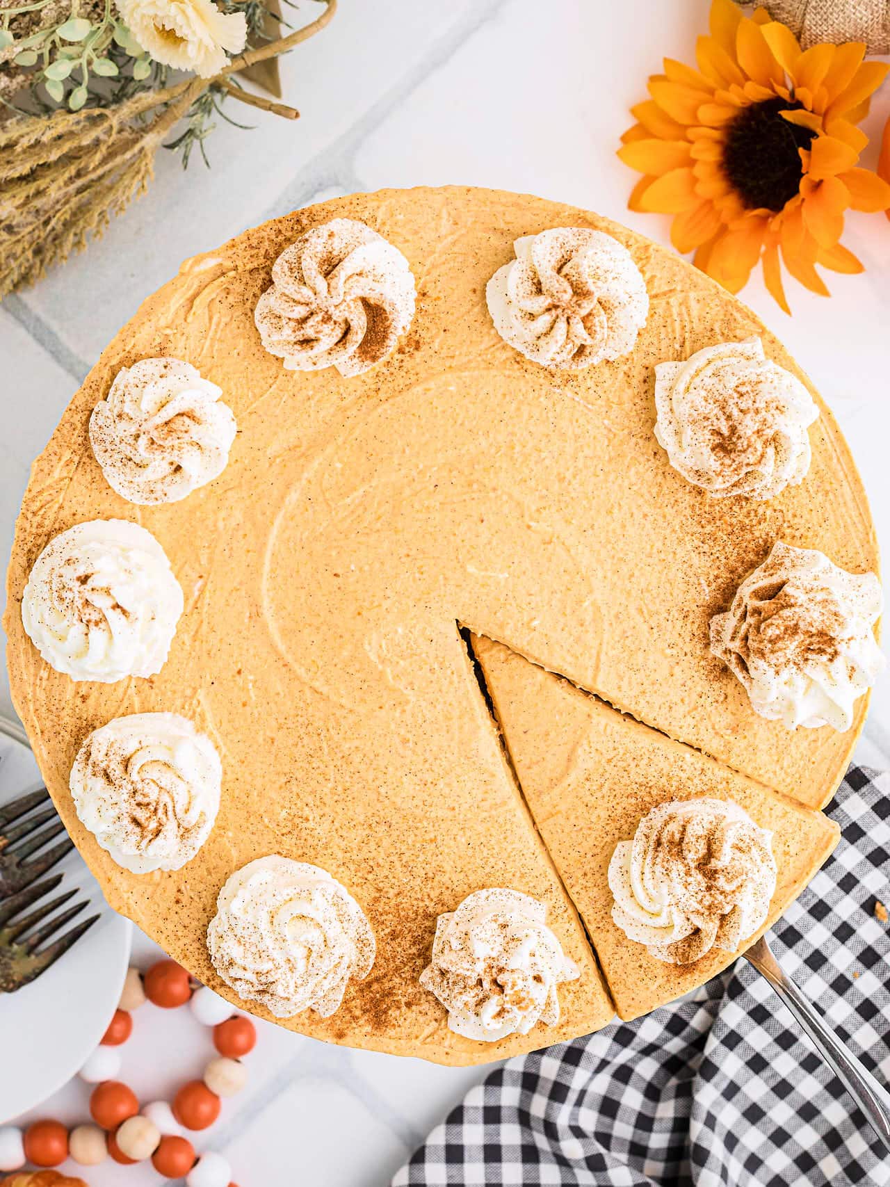 Overhead view of a whole No Bake Pumpkin Cheesecake with one slice cut and whipped cream swirls.