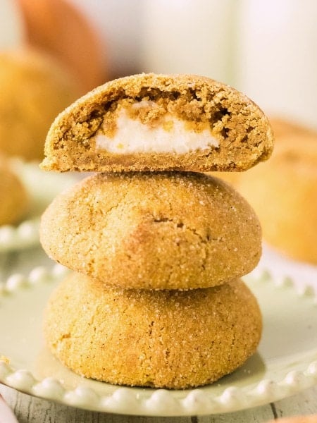 A stack of Pumpkin Cheesecake Cookies with the top cookie split open to show the creamy cheesecake center.