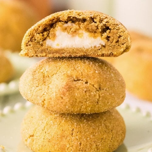 A stack of Pumpkin Cheesecake Cookies with the top cookie split open to show the creamy cheesecake center.