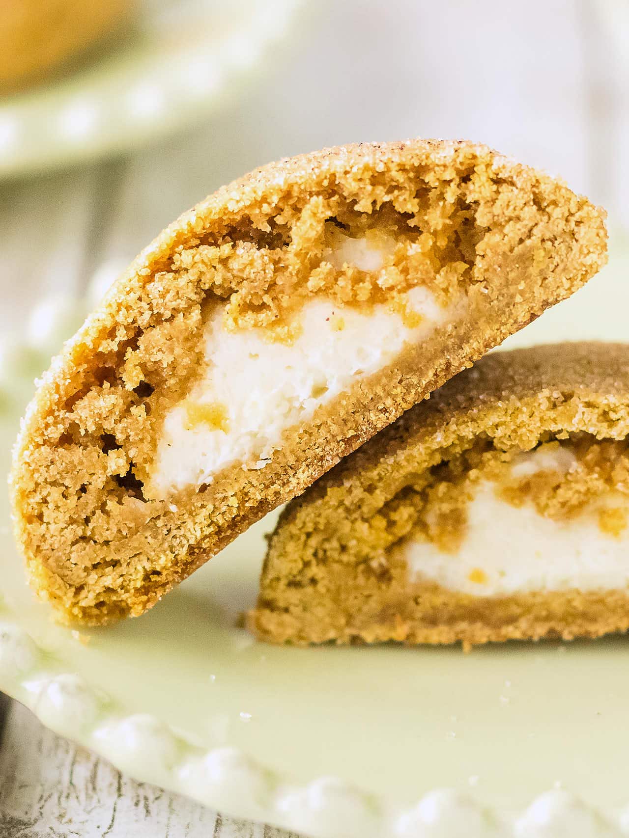 Two Pumpkin Cheesecake Cookies on a green plate with a bite taken out to show the cream cheese center.