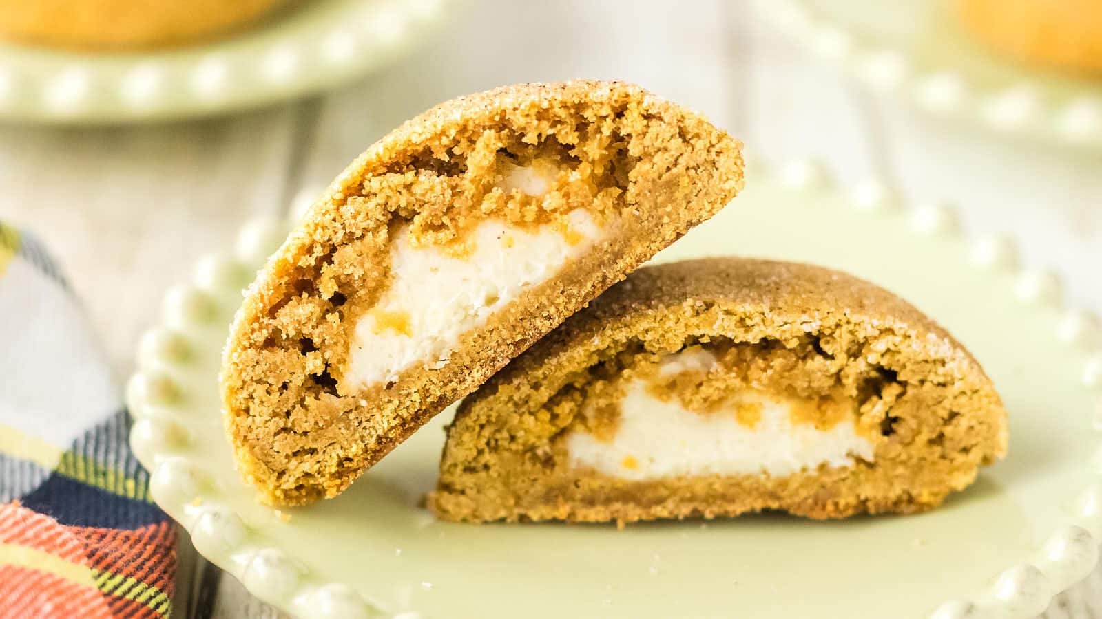 A Pumpkin Cheesecake Cookie cut in half on a green plate with both halves showing the creamy filling.