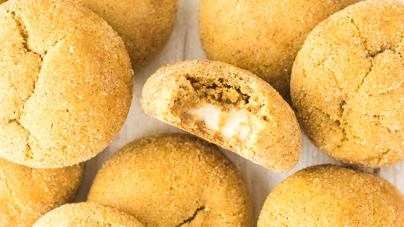 Pumpkin Cheesecake Cookies clustered together with one bitten cookie revealing the cream cheese center.