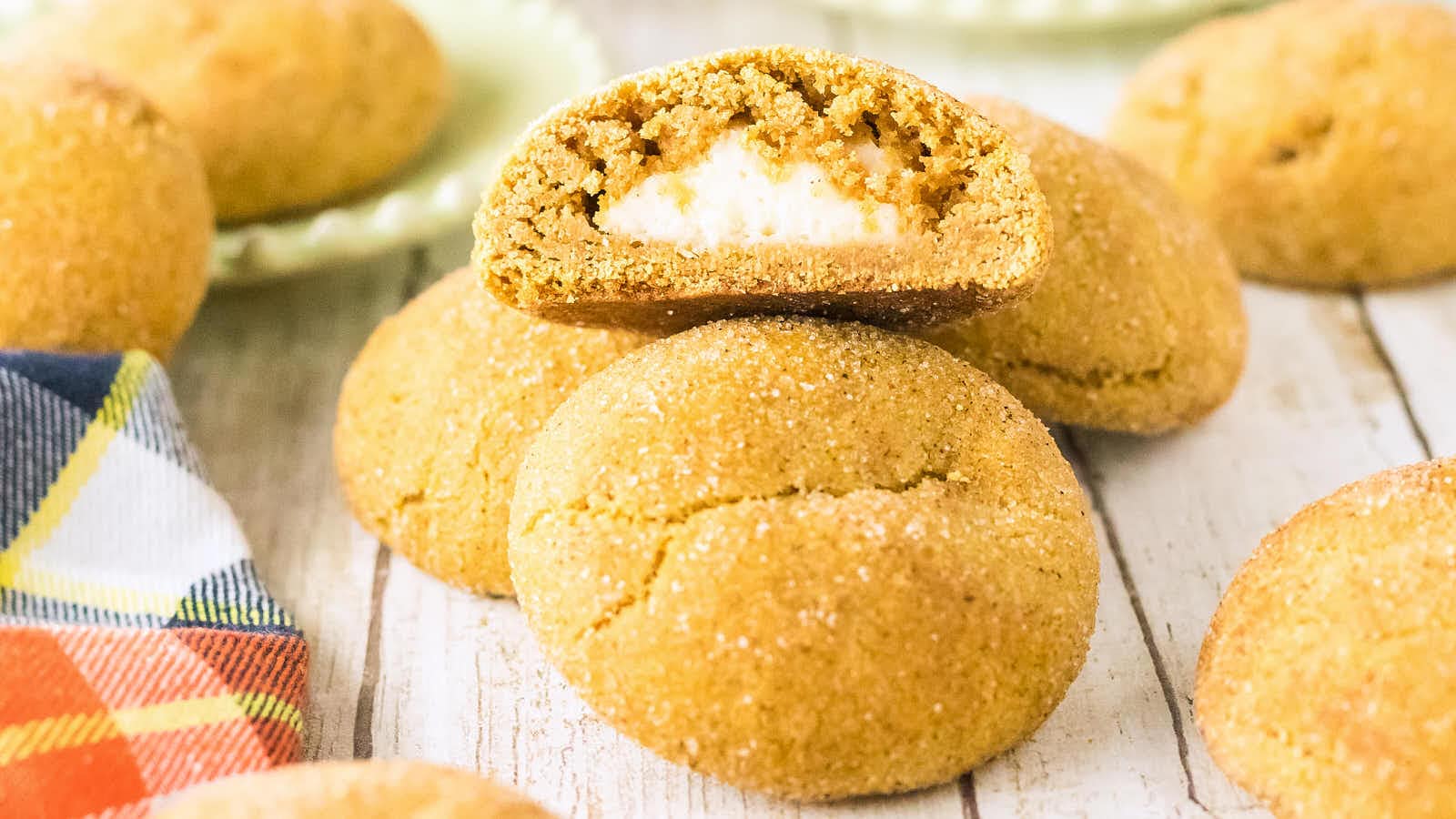 A bitten Pumpkin Cheesecake Cookie resting on top of whole sugar-coated cookies.